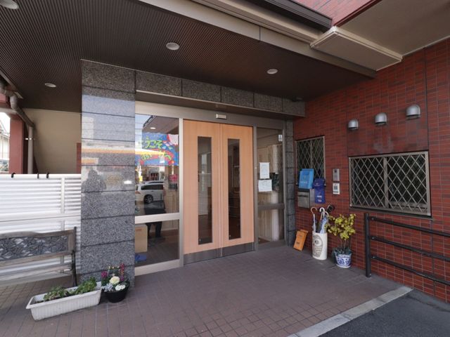 施設入り口外観 玄関 広々としたエントランスは、来訪者を穏やかに迎えます。手入れの行き届いた緑もあり、温かみのある空間を提供しています。