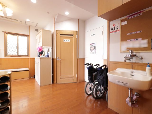 入口付近の明るい通路 ロビー 床は木目調で、手を洗うための洗面所や車椅子が設置されており、清潔で利便性の高いエントランスです。