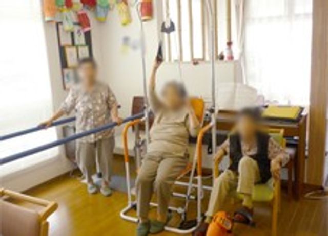 訓練を行う高齢者の部屋 機能訓練室 明るい自然光が差し込む中で、リハビリが行われています。高齢者の方も安心して利用できます。