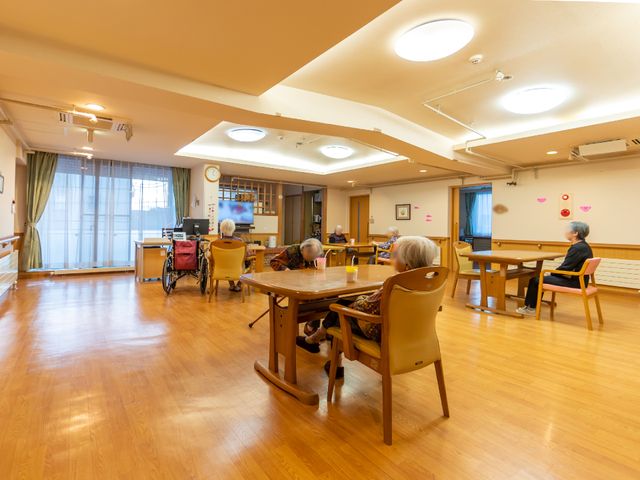 明るい食堂の一角 共有スペース 広々とした明るい空間の食堂です。椅子に座ってリラックスしながら、他の利用者との会話を楽しんでいる様子が伺えます。