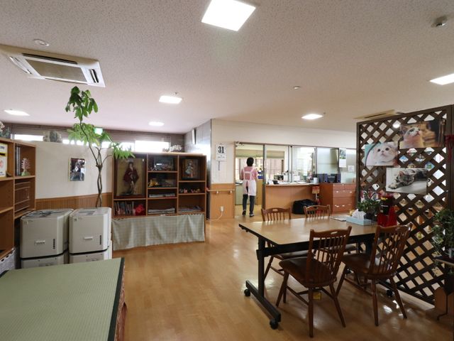 ゆったりとした共用スペース ホール 広々とした明るい食堂には心和む装飾が施され、訪れる方に安らぎを提供しています。スタッフが行き交う様子も見受けられます。