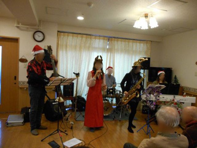 クリスマス演奏会の様子 レクリエーション 赤と緑を基調とした装飾で彩られた多目的室で、楽器を手にした方々が演奏を楽しんでいます。参加者の表情も和やかで、共に楽しいひとときを過ごされている様子です。
