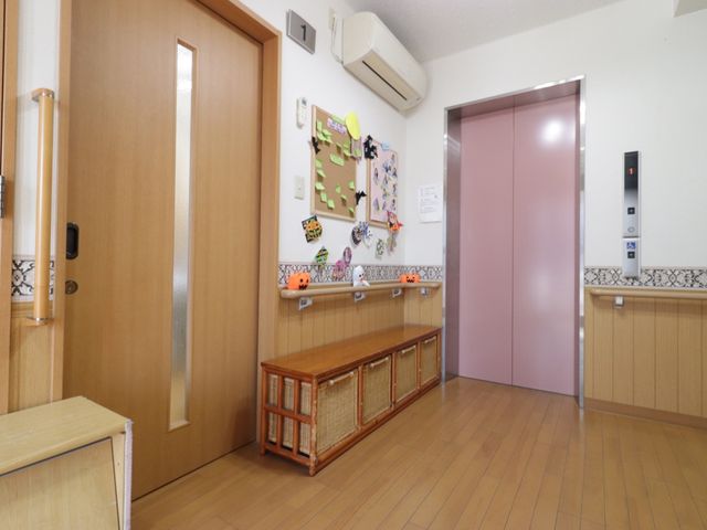 エレベーター付近の廊下 廊下 手すりが付いた明るい廊下には、椅子と掲示板が設置されており、心地よい休憩スペースを提供しています。エレベーターも完備しており、アクセスしやすい環境が整っています。