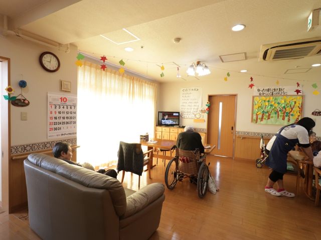 日常生活風景の共有スペース リビング ゆったりとしたソファ、明るい窓辺、居心地の良さを感じさせるリビングです。利用者同士やスタッフとのふれあいが見られ、和やかな雰囲気が伝わります。