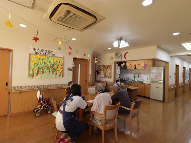 活動的な共有スペース リビング カラフルな装飾が施されたダイニングで、利用者とスタッフが椅子に座ってコミュニケーションを取っています。温かい雰囲気の中でお食事やお茶を楽しむことができる空間です。