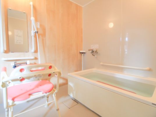 設置されたユニットバスにお湯が張られている浴室である。中には、洗い場に置かれたピンク系のバスチェアーと同色の滑り止めマットが敷かれている。