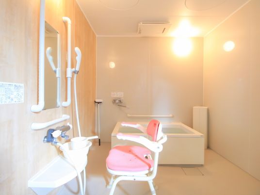 陽射しが入り明るい浴室には、浴室暖房機が天井に設置されている。洗い場の壁には、ピンク系のバスチェアーが置かれている。