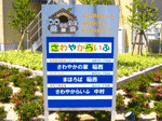 入口に立つカラフルな看板 看板 施設名が書かれたカラフルな看板が設置されています。周囲に緑が配置され、親しみやすい印象です。