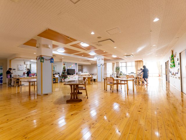 広々とした木の床の食堂 共有スペース 優しい木目の床が印象的な食堂です。スタッフと利用者が和やかな会話を楽しんでいます。