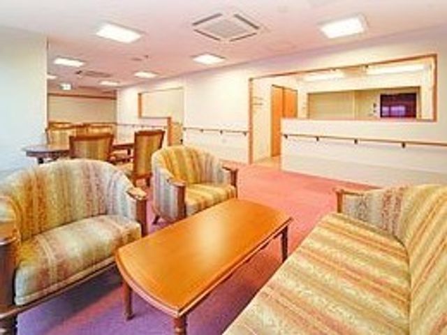 暖色系の落ち着いたロビー 談話コーナー ゆったりしたソファが配置されたロビーは、暖かみのある色合いで訪れる人をやさしく迎えます。職員とのコミュニケーションもはかりやすい開放的な設計です。