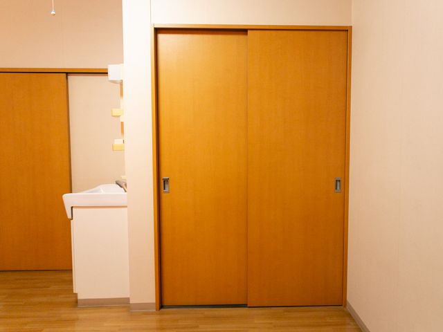 洗面台と引き戸のある居室 居室 清潔感のある洗面台と光を採り入れる木目調の引き戸が特徴の居室です。ゆったりとした生活スペースを提供しています。