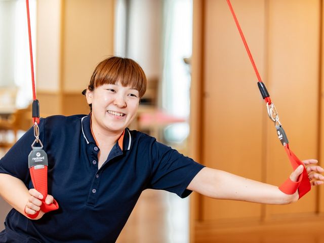 明るい訓練室での活動 機能訓練室 笑顔の職員が健康増進の為の設備を使用しています。快適な環境で体を動かせる空間です。