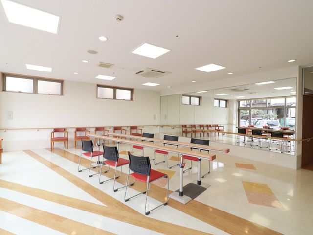 広々とした明るい機能訓練室 機能訓練室 ゆったりとした空間でリハビリに集中できる機能訓練室です。レッドとブラックのチェアがアクセントのある環境を提供しています。