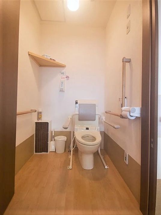 背もたれや可動式の手すりが設置されたトイレ内は広く、ごみ箱も置かれている。