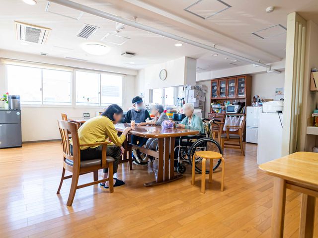共有スペースでのひと時 共有スペースA 木のテーブルを囲んで憩う人々のあたたかい光景です。そこは交流を深め、心地よい時間を過ごせる場所となっています。