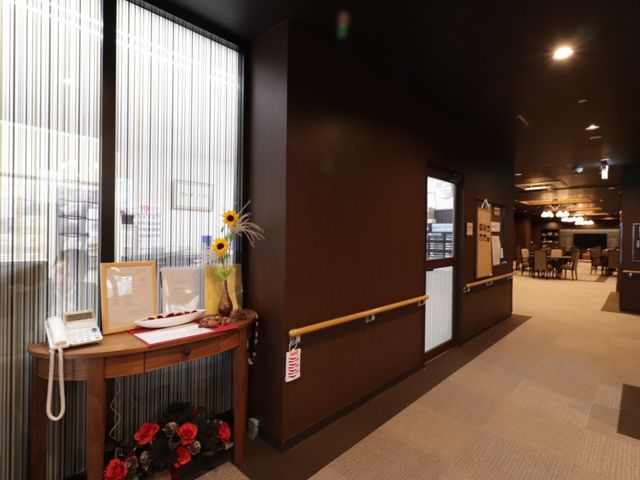 リビングスペースの入口 通路 ぬくもりのあるエントランスには、花々と案内資料が準備され、訪れる人を暖かく迎えています。明るく開放的な雰囲気で、来訪者との対話がはぐくまれる場所です。