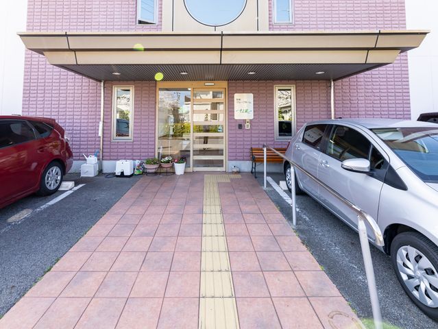 ピンクの建物のエントランス 玄関 アクセスしやすいエントランスは明るく、新たな職場として皆様を迎える準備が整っています。