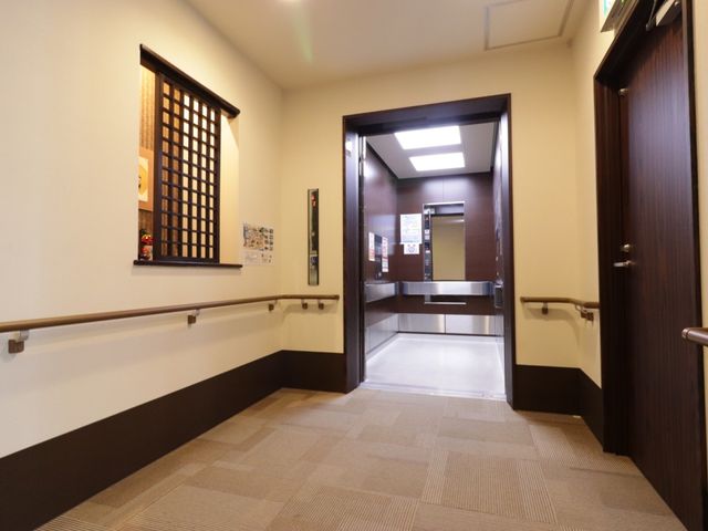 廊下とエレベーターの入口 エレベーター 広々として手すりも整った廊下です。壁には掲示物があり、情報共有にも役立っている様子が見受けられます。