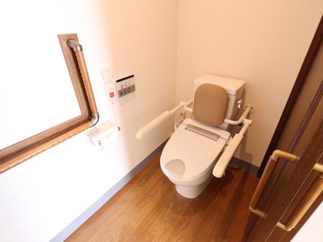 手すり付きトイレ設備 トイレ サポート用の手すりがついた清潔なトイレです。職員として安心して利用者様の介助が行える環境が整っています。
