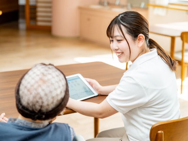 和やかな相談風景の居室 居室   自然光が差し込む空間で、スタッフが利用者に笑顔で対応しています。皆が安心して過ごせる場所です。