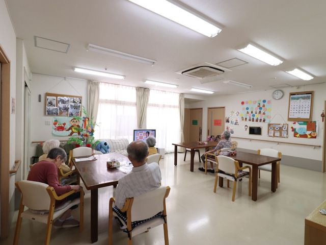 多目的室の日常風景 リビング ゆったりした空間で利用者がそれぞれの時間を過ごしています。明るく清潔感のある空間が印象的です。