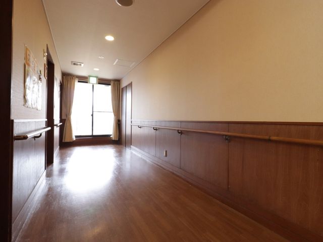 木目調の落ち着いた廊下 廊下 手すりが整った広々とした通路は、どなたでも安心して歩けるバリアフリー設計です。明るい窓辺からは柔らかな日差しが差し込みます。
