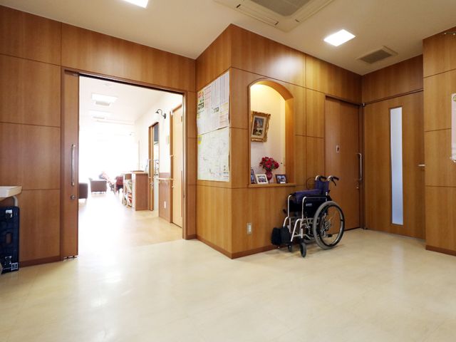 廊下にある車椅子 エントランス2 広々とした廊下には明るい光が差し込み、壁には掲示物があります。車椅子の置かれた様子から、利用者の快適な移動が考えられていることが伺えます。