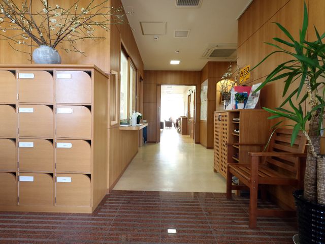 廊下の快適な空間 エントランス3 木のぬくもりが感じられる廊下は、開放感のあふれる設計です。左手には各居室への郵便物を分けるポストが設置されており、清潔感のある環境が保たれています。