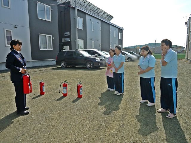 消火器訓練の様子 外観 外観   建物の前で職員が消火器の使い方を確認しています。日頃から安全対策を学ぶ様子がうかがえます。