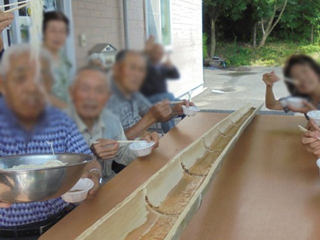 流しそうめんを楽しむ中庭 中庭 自然が感じられる中庭で、入居者の皆さんが流しそうめんを楽しんでいます。和気あいあいとした雰囲気です。
