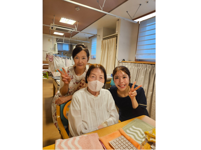 笑顔の人々と和やかな居室 居室 温かい雰囲気の居室で、スタッフと利用者が笑顔でポーズを取っている様子です。利用者同士も親しげに交流されています。