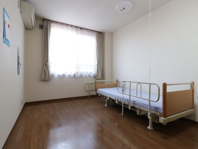 居室のベッドと窓 居室 ゆとりのある明るい居室です。手すり付きのベッドが備えられ、心地よい日差しの中で過ごせます。