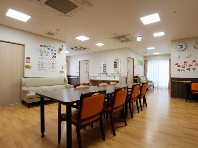 広々とした食堂の様子 リビングダイニング4 明るく開放的な食堂では、お食事を通じたコミュニケーションが生まれやすい環境です。ゆったりとしたソファも設置され、くつろぎの時間を過ごせます。