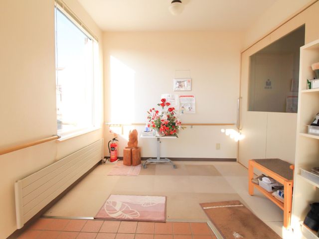 日差し入る居室の一角 玄関 床に敷かれた絨毯が温もりを感じさせ、窓からの自然光が明るい雰囲気を演出しております。手すりが設置され、安全に配慮された空間です。