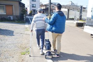 杖を使って歩く男性と若者の後ろ姿
