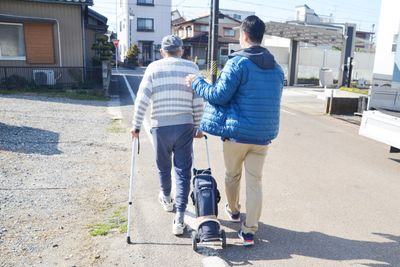 杖を使って歩く男性と若者の後ろ姿
