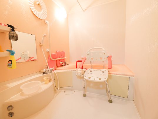 ピンクで統一されたシャワーチェアーと洗面台がある浴室