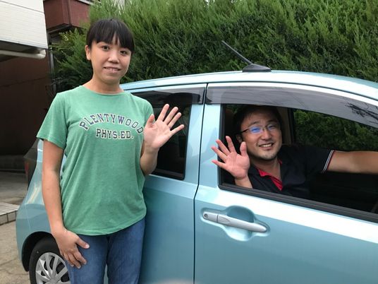 笑顔で手を振るスタッフと車