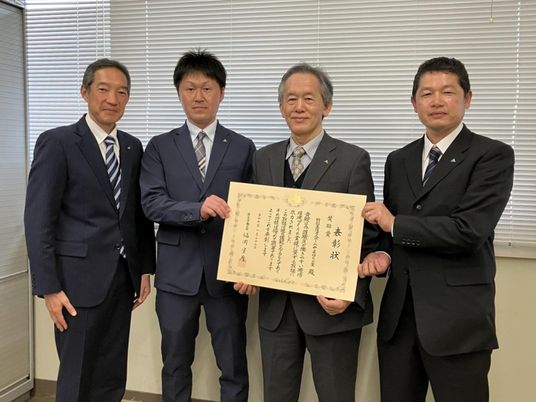 表彰状を持つ男性4人の室内  