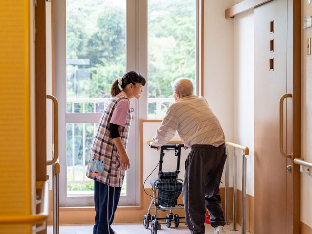 スタッフの介助風景 廊下 温かい対応で利用者さまの移動を支援しています。あなたの手で、快適な毎日を支えていきませんか？