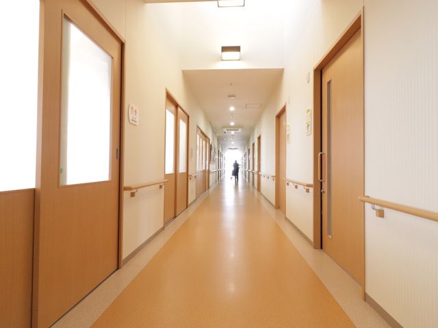 明るい廊下と歩く人影 廊下 手すりが取り付けられた広々とした廊下で、安全に歩行できる環境が整っています。ゆったりと移動できる空間で働くことができます。
