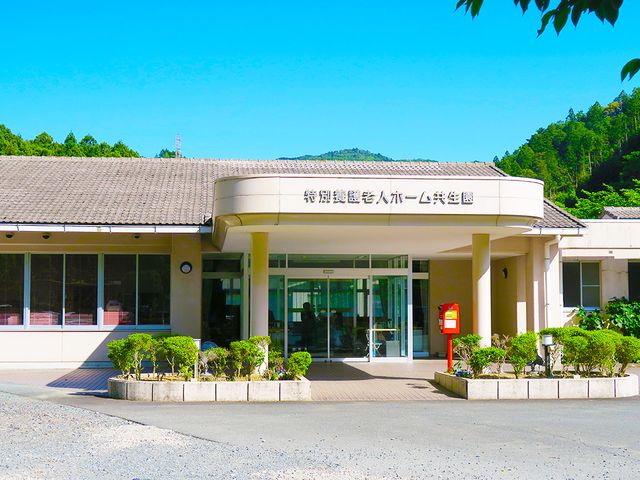 玄関の外にある建物 外観 緑豊かな環境に囲まれた建物の入口です。明るい日差しが差し込み、訪問者を優しく迎え入れます。