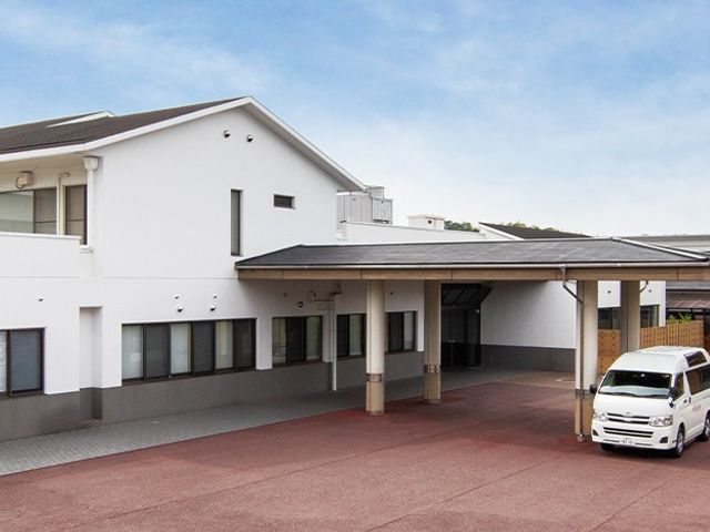 白い建物の外観 外観 広々とした駐車スペースが備わっており、車での来訪にも便利です。大きな建物と緑の調和が感じられます。
