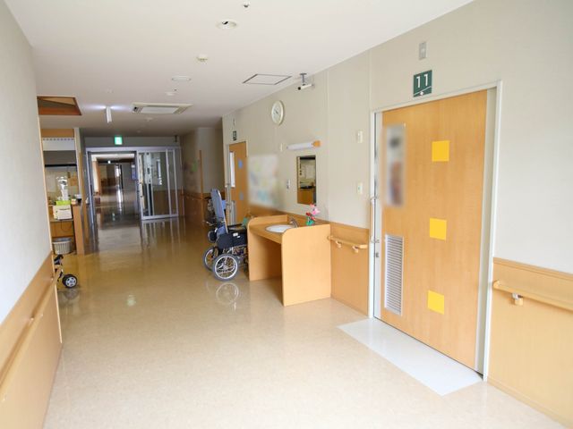 廊下と部屋の入り口 通路 広々とした廊下には車椅子が配置され、バリアフリーな構造が見受けられます。明るく清潔感のある環境が、快適な日常をサポートしています。