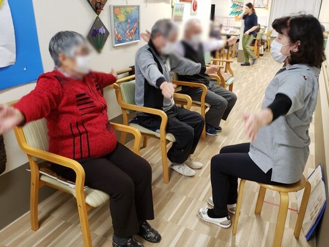 体操をする集団 ラウンジ 住人が椅子に座りながら体操を行い、リラックスした雰囲気が感じられます。