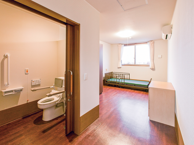 居室とトイレのある部屋 居室   明るい居室に介護用ベッドが置かれています。隣には手すり付きのトイレがあり、動線がわかりやすいです。