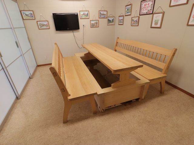 木製テーブルとベンチの部屋 談話室 温かみのある木製のテーブルとベンチが設置された休憩スペースです。壁にはアートが飾られ、心地よい環境で過ごせるようになっています。