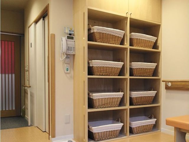 整理棚とドアの居室 更衣室 整然と並んだ籠の収納棚と落ち着きのある色合いが特徴の居室です。快適で清潔感のある生活空間をお求めの方におすすめです。
