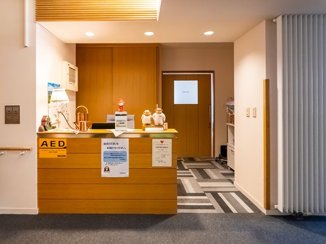 受付の様子が見える空間 受付 温かみのある照明と木目調の受付カウンターが迎えてくれる、心穏やかに過ごせる環境です。安全面も配慮されたAED設置場所も備えており、安心してご就業いただけます。
