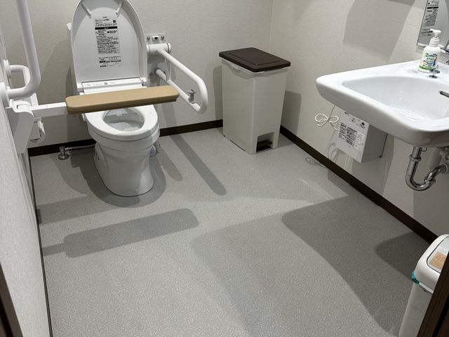 青空の下の建物外観 トイレ 手すり完備で住み心地の良いトイレの清掃など、ご利用者様の快適性を守るお仕事です。